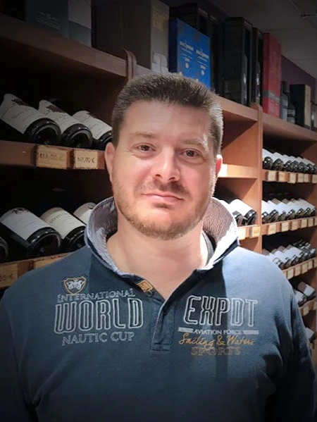 Guillaume Nicolas, caviste expert chez As du Vin à Dijon, posant devant les rayonnages de bouteilles de vin de la boutique.