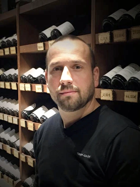 Castells François-Xavier, caviste expert chez As du Vin à Dijon, posant devant les rayonnages de bouteilles de vin de la boutique.